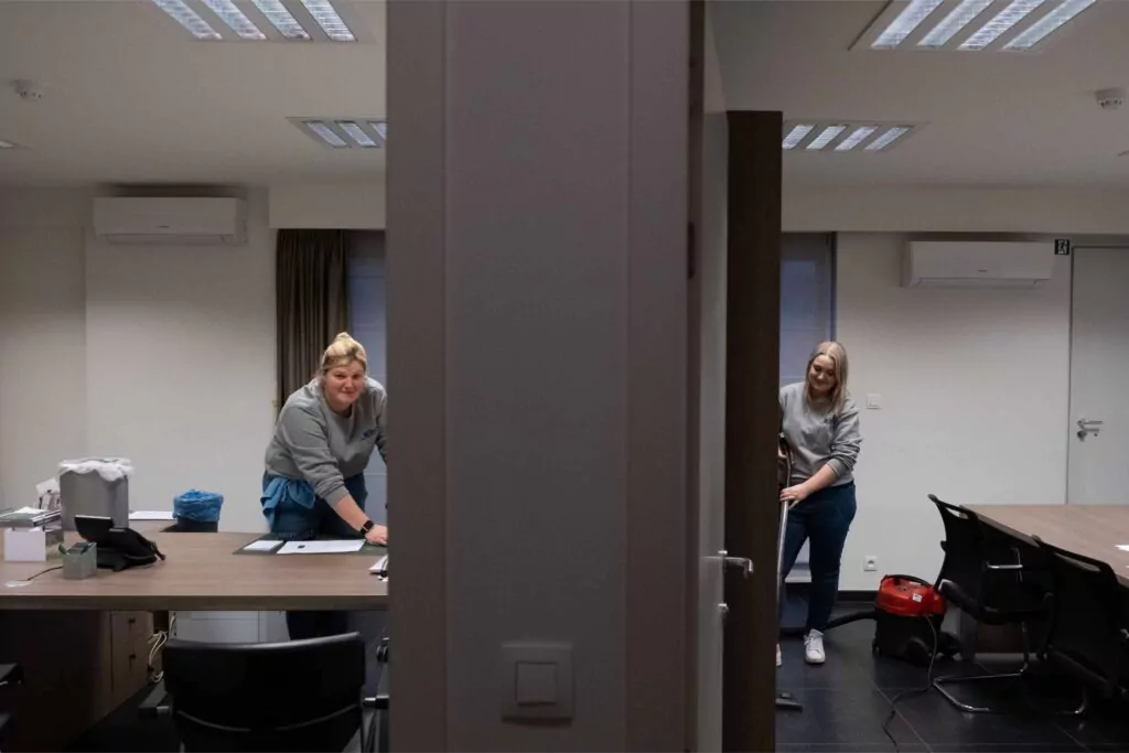Three professional cleaners in bright green overalls standing confidently with cleaning equipment in modern home interior with gray walls