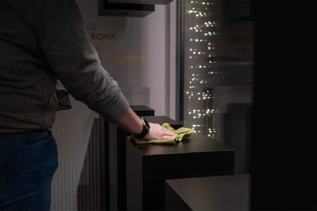 Three professional cleaners in bright green overalls standing confidently with cleaning equipment in modern home interior with gray walls