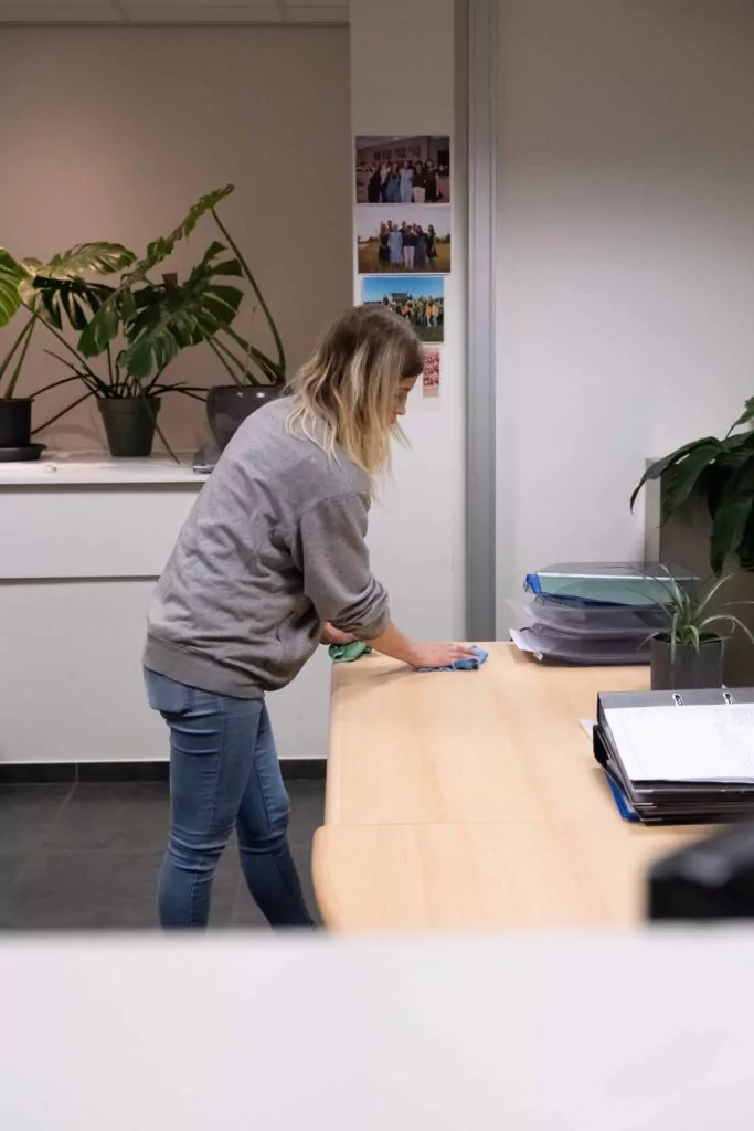 Three professional cleaners in green and red overalls working in a modern kitchen, mopping the floor, and cleaning high walls and windows.