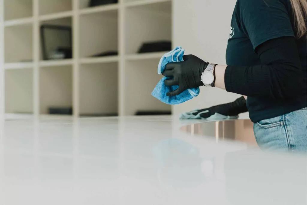 Three professional cleaners in green and red overalls working in a modern kitchen, mopping the floor, and cleaning high walls and windows.