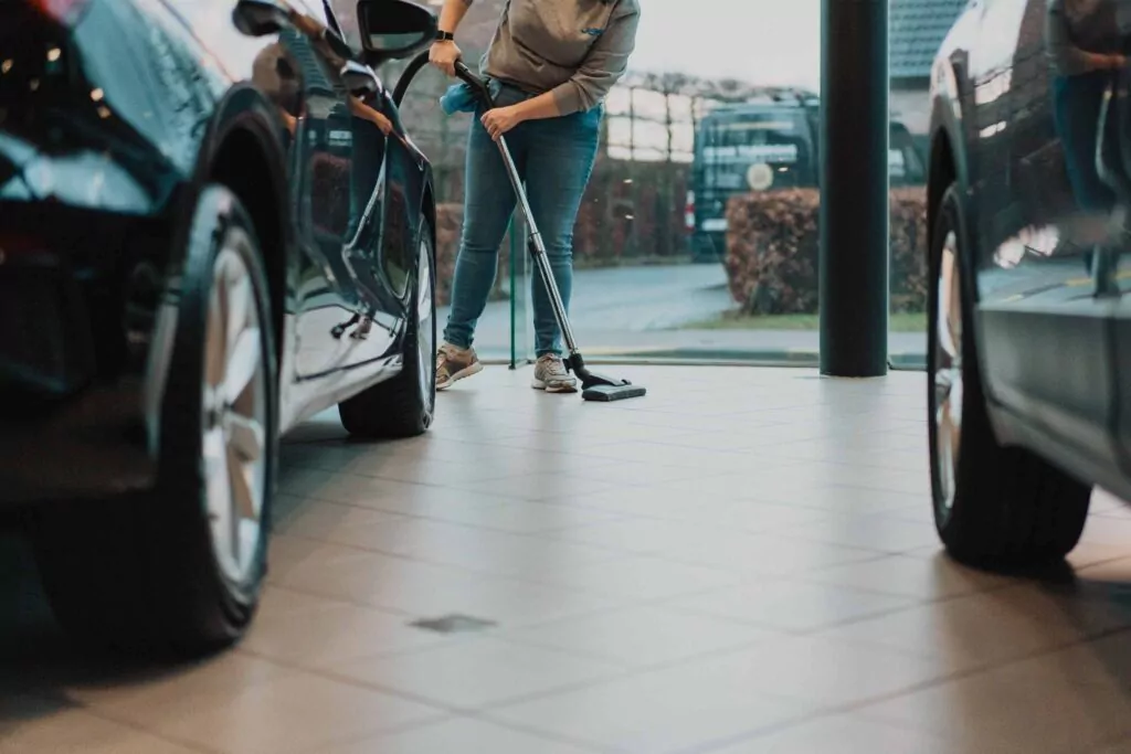 Three professional cleaners in green and red overalls working in a modern kitchen, mopping the floor, and cleaning high walls and windows.
