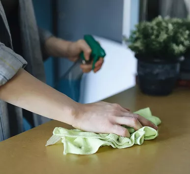 Close-up of a person wearing a striped shirt wiping a smooth, light-brown countertop with a light green microfiber cloth.